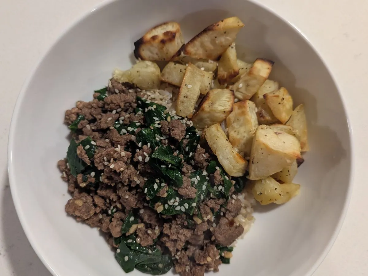 White bowl with seasoned ground beef and spinach over rice alongside roasted Japanese sweet potato chunks topped with sesame seeds
