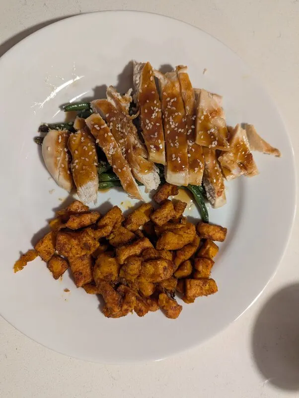 Sesame chicken with sweet potatoes and greens on a white plate
